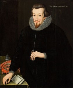 A thin-faced, bearded man in dark clothes, with papers and an official red, embroidered, dispatch bag beside him.