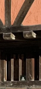 A small black and white cat peering out of the unglazed window of a Tudor house.